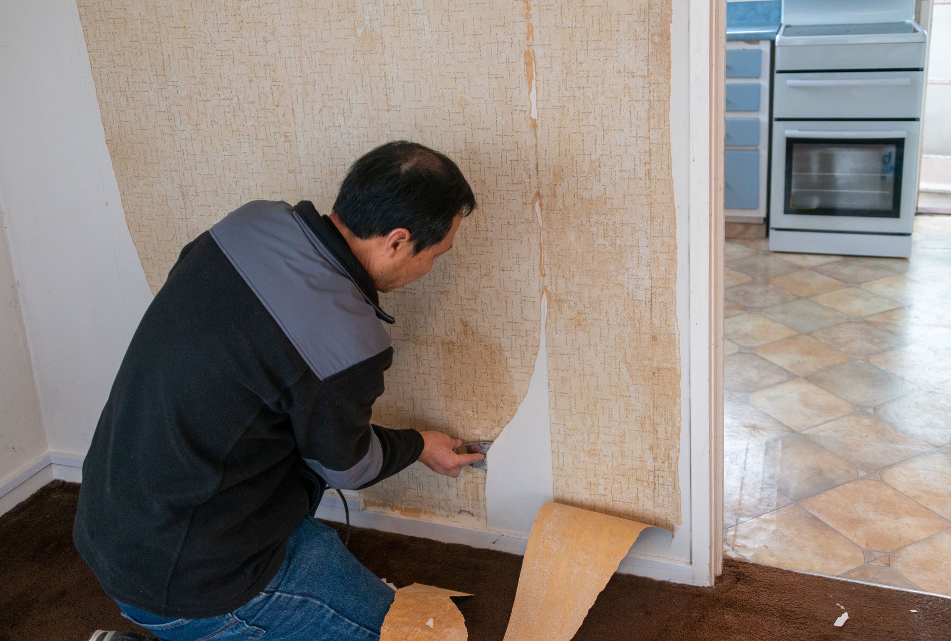 Man removing wallpaper inside an old house. Home interior renovation project.